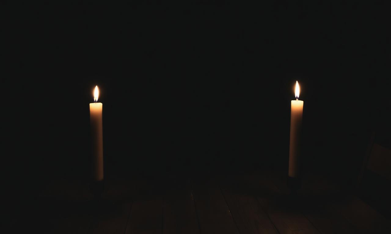 Two candles burning on opposite sides of a wooden table at night